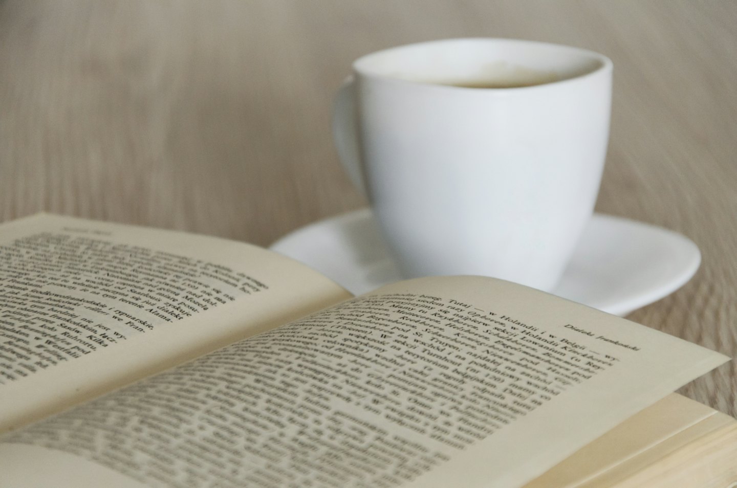 Un libro aperto giace su una superficie di legno accanto a una tazza di caffè.