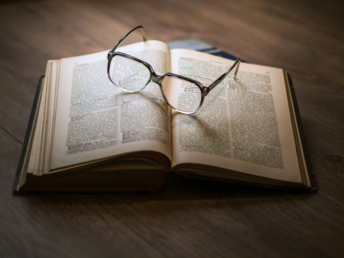Libro antico con occhiali da lettura su un tavolo di legno.