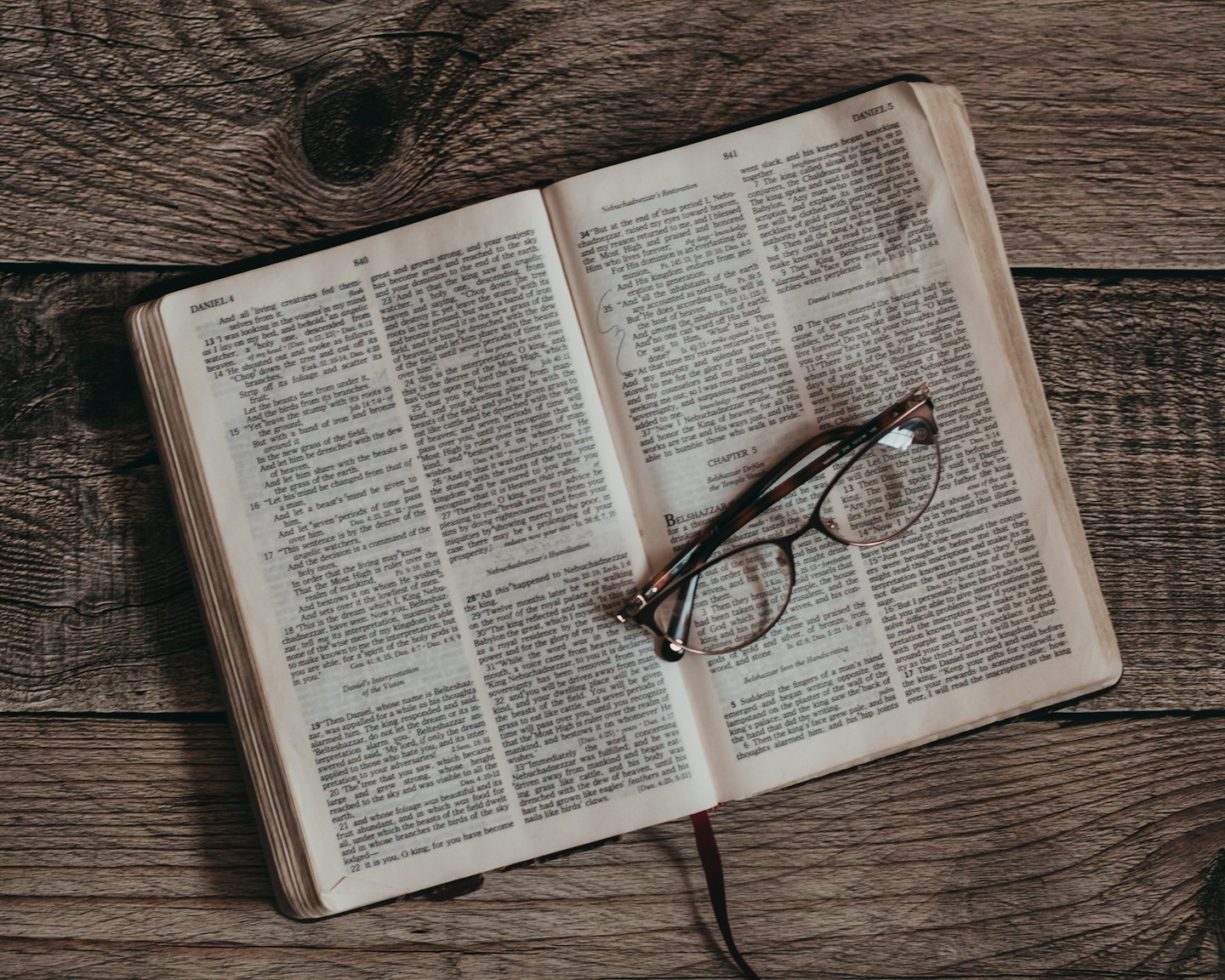 Occhiali da vista tartarugati appoggiati su un libro aperto su un tavolo di legno.